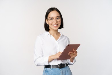 image of young asian woman, company worker in glasses, smiling and holding digital tablet, standing over white background