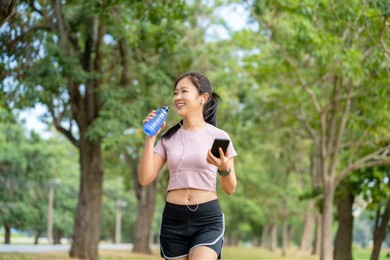 asian attractive sporty woman drinking water from a bottle after jogging or running while she sitting in park.