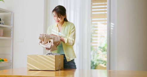 asian woman is sort old clothes waste in garbage box for recycling at home
