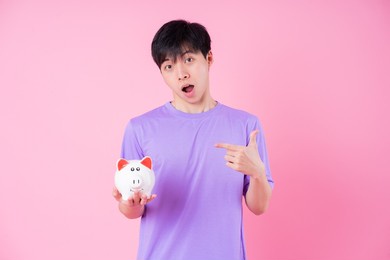 young asian man holding piggy bank on pink background