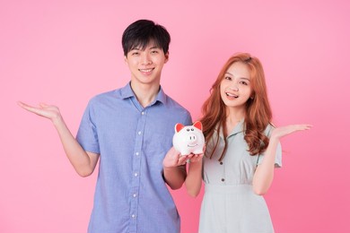young asian couple holding piggy bank on pink background