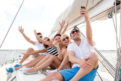 vacation, travel, sea, friendship and people concept - smiling friends sitting on yacht deck and making selfie