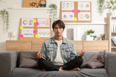 clam of asian young man doing yoga lotus pose to meditation and relax on couch during work online at home.happiness male break after worked close him eyes and deep breath with yoga so peaceful.