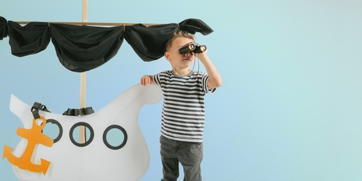 little child boy playing with cardboard ship on blue wall background