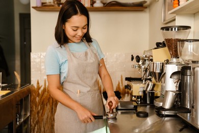 young asian barista wearing apron smiling while making coffee in cafe