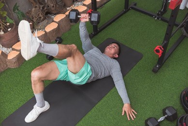 a fit asian man in a gray sweater does alternating floor presses with leg raised. chest workout at his home gym.