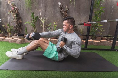 full situps with dumbbells and alternate cross punch. performed by a fit asian guy lying on a black mat. intense reciprocal exercise at a home gym. side view.