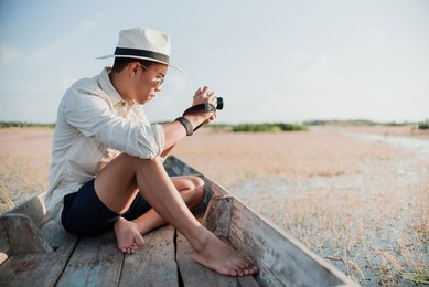 asian tourism concept, asian man sitting on a boat and taking pictures of lake water in thailand.