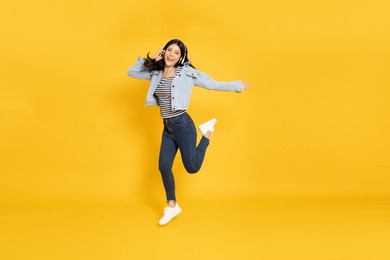 young asian woman listening favourite music with wireless headphones and dancing isolated on yellow background