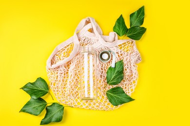 reusable glass bottle for water on yellow background.may bottle.cotton bag,glass bottle and bamboo tubes.let's go shopping.ecological, natural materials.the concept zero waste.the view from the top.