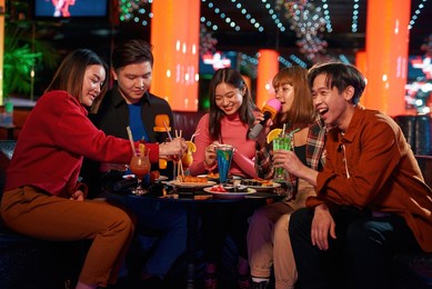 singing songs and eating sushi rolls at karaoke club, eating sushi rolls using bamboo sticks, enjoying friendship together in bar, concept of party, fun, holiday, relaxation, spend day-off