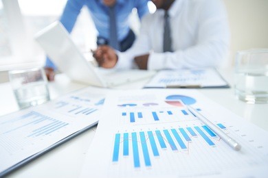 documents with chart and graph and pen on background of two employees working