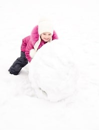 cute smiling little girl makes snowman in winter day outdoor