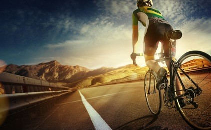 cyclist riding a bike on an open road to the sunset 