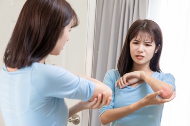 asian woman has dry skin and scratches her arms in front of mirror at home