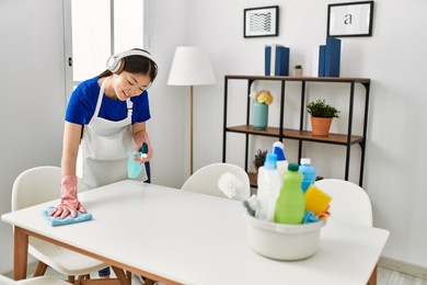 young chinese housewife cleaning and listening to music using headphones at home.