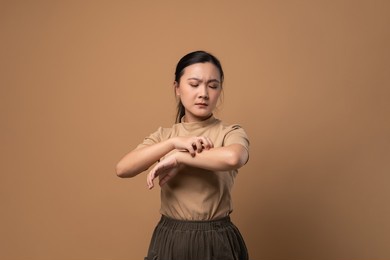 asian woman was sick with irritate itching her skin, scratching her skin, standing isolated on beige background.