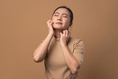 asian woman was sick with irritate itching her skin, scratching her skin, standing isolated on beige background.