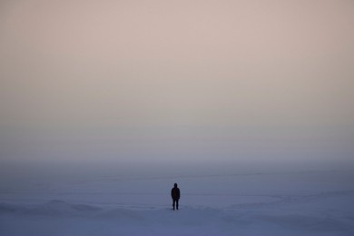 a lonely man looks into the distance in the cold surrounded by an icy desert and endless ice. black and white. loneliness. boredom and despair