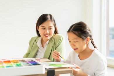 beautiful teacher happy, smile, look at young child fun painting color in education classroom, select focus at teacher. asian beautiful children happy and fun color painting education in small school