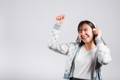 woman excited smiling listening to music radio in bluetooth headphones and dancing with smartphone studio shot isolated white background, happy asian young female karaoke online app in mobile phone