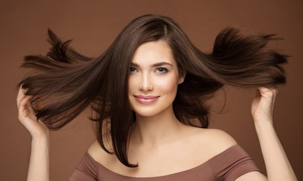 hair beauty model. brunette woman with straight hairstyle flying on wind over dark beige. young smiling girl with smooth skin make up