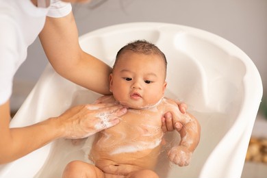 calm of asian newborn baby bathing in bathtub.mother bathing her son in warm water.happy adorable newborn infant smile in tub relax and comfortable.newborn baby care concept