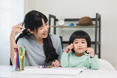 mom teaching son how to painting with crayon color on book or doing homework. happy asian boy painting with crayon and colored pencil with his mother in living room at home.  family concept.