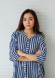 horizontal portrait shot of an attractive asian woman in casual long sleeve blue and white striped shirt looking at camera and crossed arms in studio with white background and copy space on side