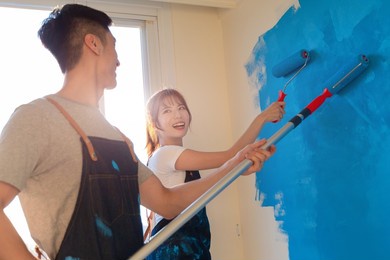 close up of young asian couple decorate home - they painting wall with blue color together and having fun