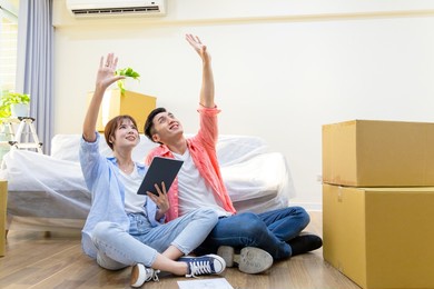 asian young couple have interior design discussion for their new home with digital tablet - they sitting on wooden floor and having dreams in house