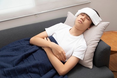 young asian teenage boy feeling sick in blanket with white towel on the forehead.