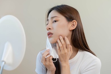 dermatology, puberty asian young woman, girl looking into mirror, allergy when wear mask and cosmetic, show squeezing pimple spot for removing from face.beauty care from skin problem by acne treatment