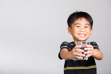 little cute kid boy 5-6 years old smile drinking fresh water from glass in studio shot isolated on white background, asian children preschool, daily life health