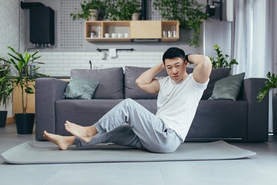asian at home doing fitness, a man sitting on the floor shakes his abdominal muscles
