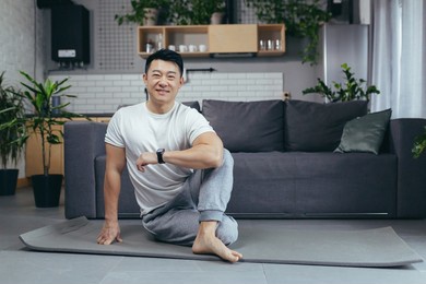 portrait of a happy asian man doing fitness and doing morning exercises in the morning, man sitting on a sports mat and looking at the camera motivated