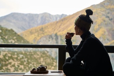 asian woman sitting on balcony drinking tea enjoying mountain scenery with autumn foliage