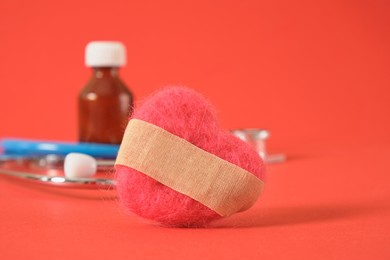 a heart made of natural wool with a glued adhesive plaster, medical medicines and tools on a red background diseases of the cardiovascular system concept