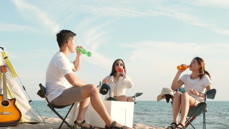 happy friends with drinks in camp and laughing together in holidays on sand beach near camping tent vacation time at sunset, young asian group woman and man in summer travel outdoor