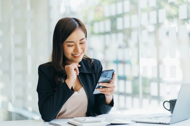 asian businesswoman in formal suit in office happy and cheerful during using smartphone and working