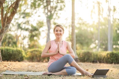 beautiful young asian woman healthy in sportswear workout practice yoga online with tablet in nature park outdoor under sunset. healthy lifestyle and relaxation.