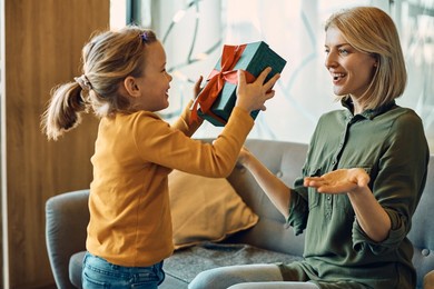 caring little girl surprising her mother with a present for mother's day.