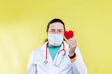 a doctor in a white coat and mask holds out a red heart. the concept of proper treatment and faith in a good future. bracelet in the colors of the german flag. 