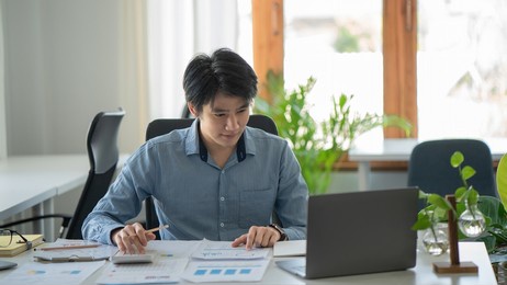 asian businessman works in the office, calculates the report, the financier on paper works, uses the laptop and the calculator