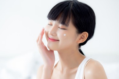 beautiful young asian woman happy applying cream or lotion with moisturizer to skin on face, beauty asia girl applying skincare touch facial with cosmetic makeup, skin care and health concept.