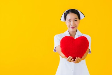 portrait beautiful young asian woman thai nurse show heart pillow shape and work at clinic or hospital on yellow isolated background