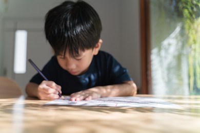 asian boy about 5 years old doing his homework, drawing and painting picture with color pencil