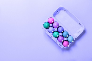 package of chicken eggs with white fluffy tails as a easter bunnies painted in various colors on lilac background. copy space. banner. religion holiday concept. mockup design. neon minimalist style.