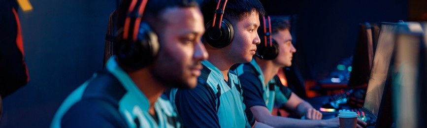 group of focused esports players sitting together in front of computer monitors and playing video game in internet cafe