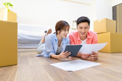 asian young couple have interior design discussion for their new home with digital tablet - they lying on wooden floor in house
